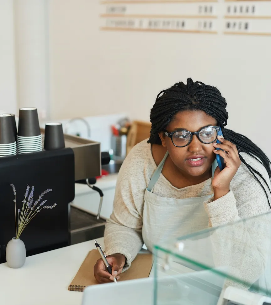 Café owner in apron answers phone call and takes notes behind the counter