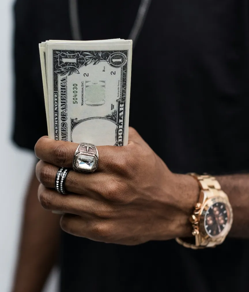 Gold watch on wrist holding crisp dollar notes like playing cards